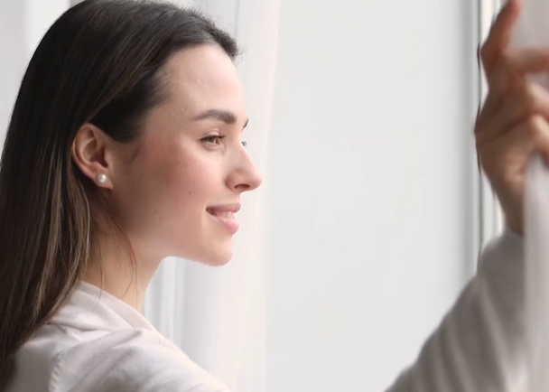 Woman in a white shirt standing in front of a window with light filtering through.