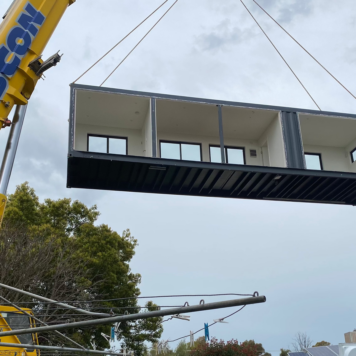 Container being lifted by a crane with 'Barcon' branding against a cloudy sky.