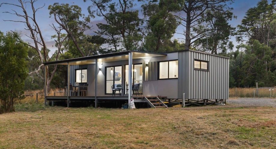 Modern tiny house with large windows surrounded by trees in a rural setting