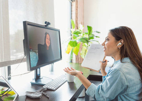 Woman on a video call at a desk with a computer and tablet.